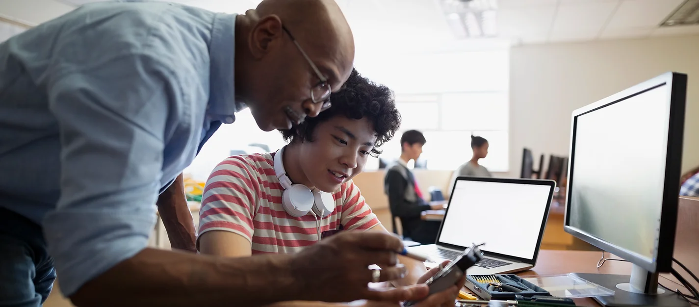 African American man mentoring a young teenaged Latino boy with an electronic device.